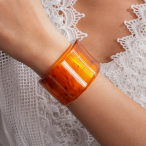 Detailed close-up of a chunky amber marbled resin elastic bangle worn on a wrist