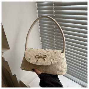 Détail d'un sac à main en paille avec broderie florale et boucle nœud dorée