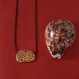 Detail of leopard print pendant with gold frame on black cord against dark red backdrop