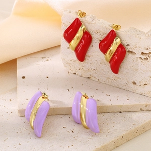 Détail de boucles d'oreilles dorées 18K avec émail rouge et violet sur marbre