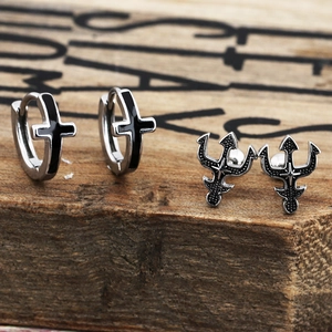 Detailed close-up of punk style cross and trident earrings on rustic wood background