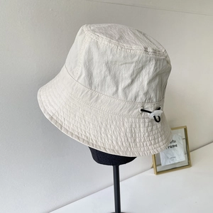 Detail of adjustable black drawstring and plastic buckle on a beige nylon bucket hat
