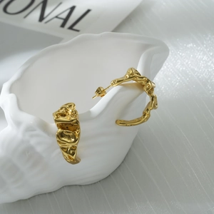 Detail of gold irregular textured earrings resting on a white shell-shaped dish