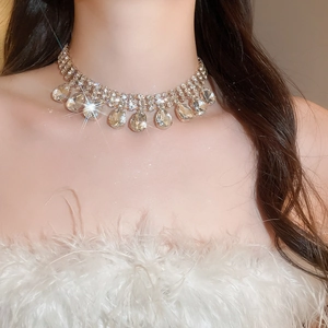 Close-up of sparkling diamond teardrop tassel necklace on model with layered gold chains