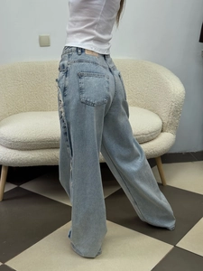 Detail view of high waist wide-leg jeans featuring side fringe and distressed raw edges
