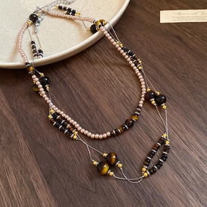 Detail of layered bohemian necklace with tiger eye beads and floral pendant on wood