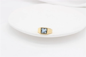 Macro shot of gold wide band signet ring featuring a square light blue gemstone on white stone