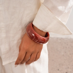 Detail of a wide deep red resin geometric bangle with white marble textures on model