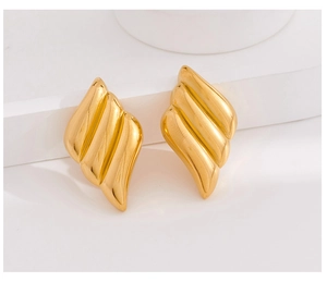 Macro detail of gold plated wing shaped earrings with a polished 3D streamlined texture