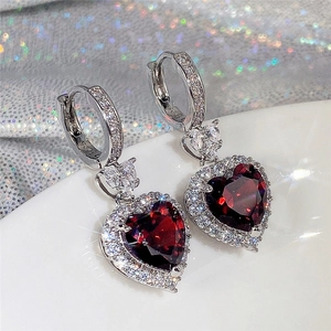 Macro shot of silver earrings with heart-shaped red gems and pave-set diamonds