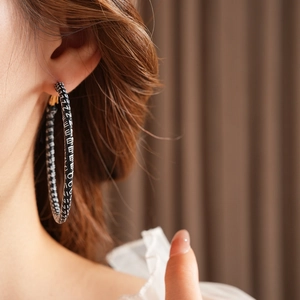 Close-up of retro silver needle hoop earring featuring a black and white letter texture