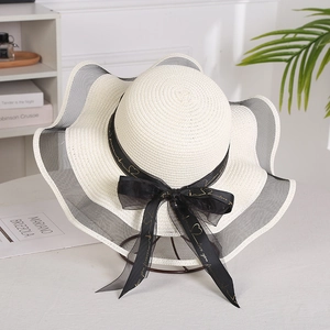 Detail of wide brim straw hat with wavy mesh trim and golden lettered black ribbon bow