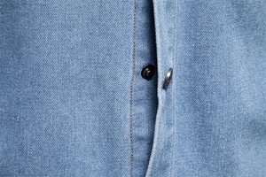 Detailed close-up of light blue denim shirt placket with orange stitching and metal buttons