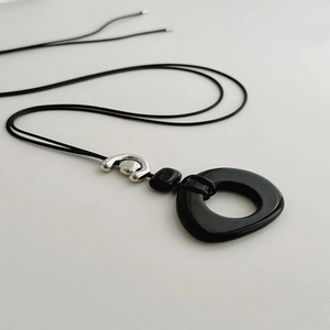 Close-up of a minimalist necklace featuring a black irregular ring pendant on a sleek cord