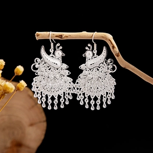 Detailed close-up of peacock dangle earrings with cloisonné silver-plated tribal patterns