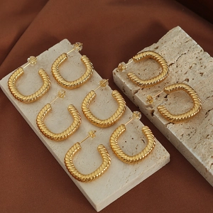 Minimalist square geometric twisted gold hoop earrings for women on a textured stone surface