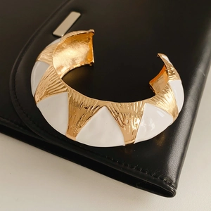 Detail of vintage gold-tone oval open bangle with white enamel and geometric texture
