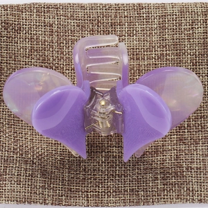 Macro detail of a purple acetate hair claw clip with bow design on a textured fabric base
