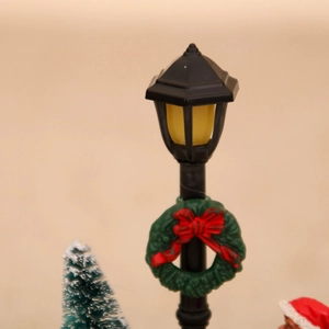 Close-up of a miniature Christmas street lamp with a festive wreath and small pine tree