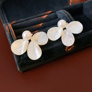 Macro detail of mother-of-pearl flower earrings with gold finish on navy velvet