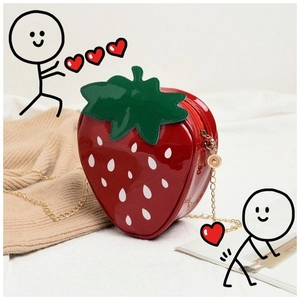 Close-up of strawberry shaped red patent leather bag with gold chain on soft background