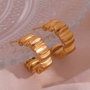 Détail de boucles d'oreilles dorées en forme de C avec finition en métal brossé mat