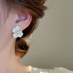 Macro side view of a minimalist gold-plated flower stud earring worn by a model