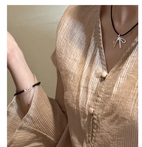 Detail of s925 silver bow pendant necklace and black beaded bracelet on a model