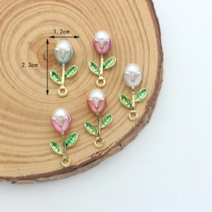 Handmade enamel tulip flower charms with pearl accents on rustic wood background