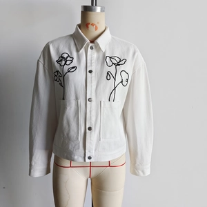 Close-up of white canvas jacket featuring intricate black floral embroidery on front pockets