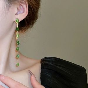 Detail of elegant long green beaded tassel earrings with gold chain on model