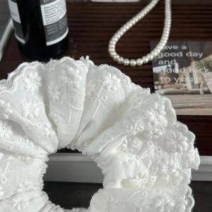 Close-up of a white lace scrunchie featuring 3D floral embroidery and layers of lace