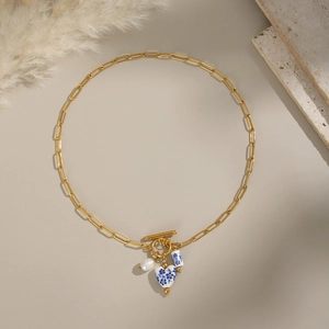 Close-up of heart-shaped blue and white porcelain pendant with pearl on a gold chain