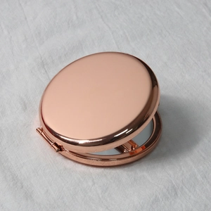 Detail of rose gold round metal mirror with high-gloss finish on white fabric