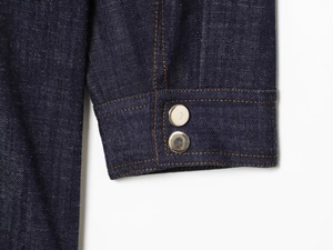 Detail of dark blue denim sleeve with silver metal buttons and contrast orange stitching