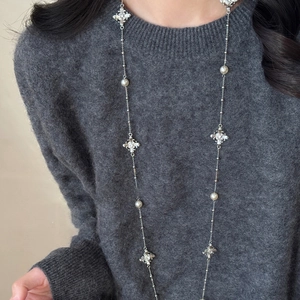 Détail du collier de perles avec pendentif croix en œil de tigre sur pull gris