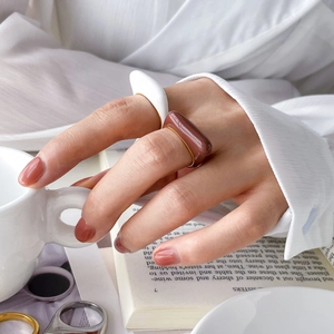 Detail of stacked white and reddish brown enamel geometric rings on fingers