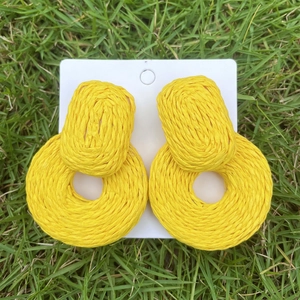 Detailed view of yellow woven raffia earrings on natural green grass background