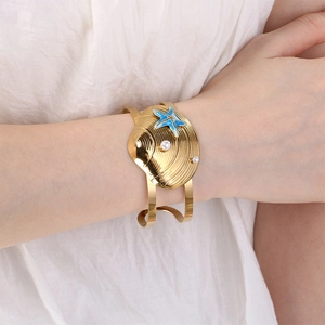 Detail of gold seashell cuff bracelet featuring blue starfish and white pearls on wrist