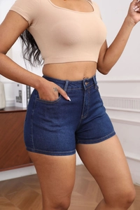 Detail view of high-waisted dark blue denim shorts with front button and side pockets