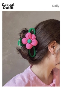 Vue détaillée de la fleur en tissu rose et de la pince à cheveux verte sur cheveux bruns