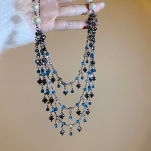 Detail of multilayer tassel necklace with blue crystals, heart pendant and white pearls
