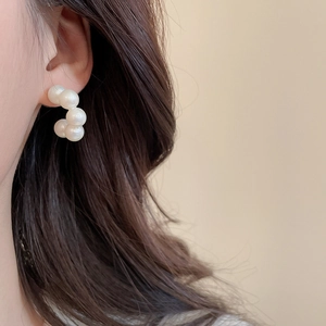 Close-up of elegant C-shaped pearl earrings on model highlighting the white luster