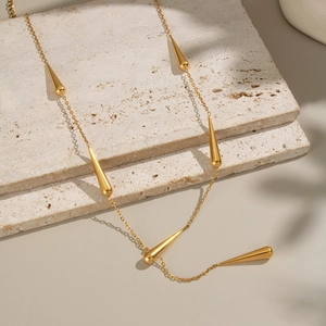 Détail du collier à pampilles gouttes dorées sur un support en pierre beige