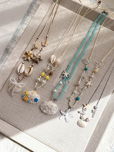 Detail view of summer starfish and shell pendants on wax cord necklaces in a linen tray
