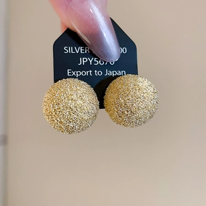 Close-up of golden spherical stud earrings featuring a textured crushed gold frosted finish