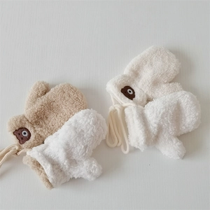 Detailed view of plush beige and white gloves featuring cute brown bear embroidery