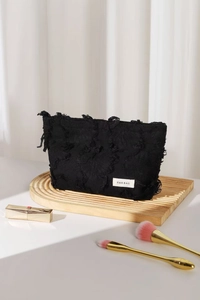 Close-up of black frayed linen makeup bag with H&R brand label and premium zipper detail