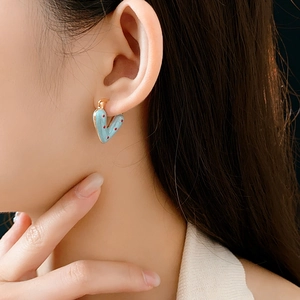 Close-up of light blue enamel heart hoop earrings with red polka dots and gold trim