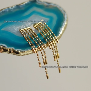 Close-up of gold fringe earrings featuring hanging chains and beads on a teal agate slice